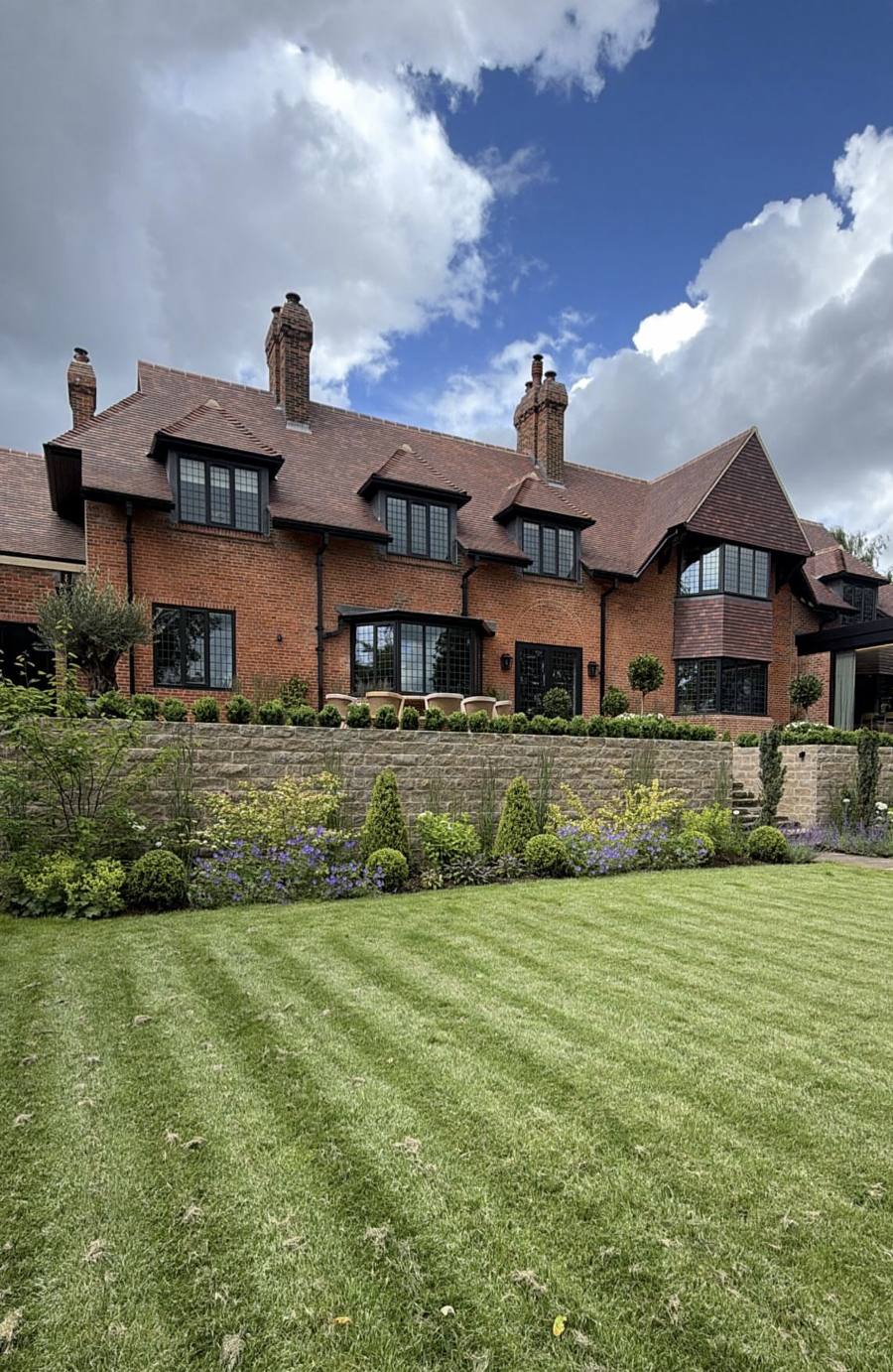 Red-brick house above a new stone retaining wall and planted borders